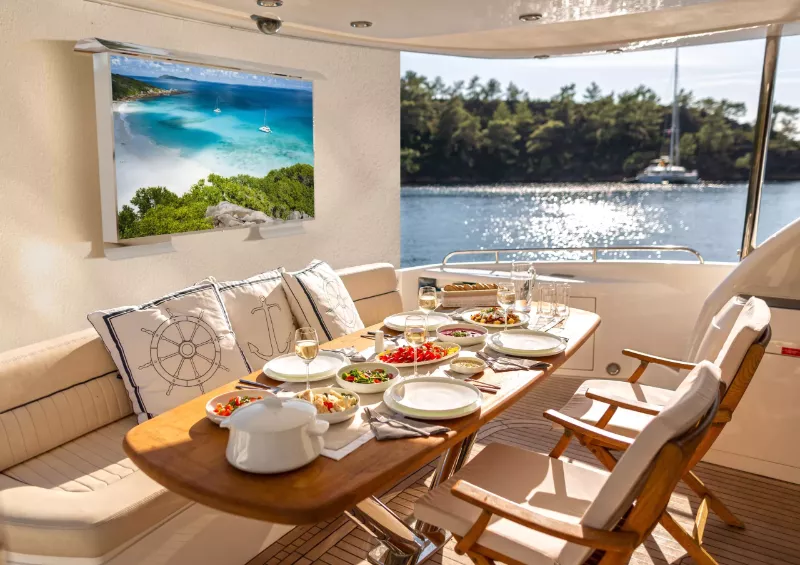 A shiny day with appealing dining table on a yacht and a wall mounted cosmos marine outdoor TV.