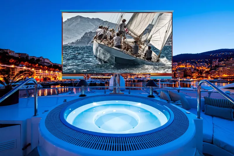  A large screen of floor mounted cosmos marine outdoor TV featuring boat in the background.